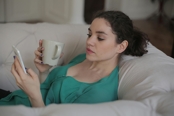 Woman relaxing on couch, holding mug, reading a smartphone. Woman relaxing on couch, holding mug, reading a smartphone.