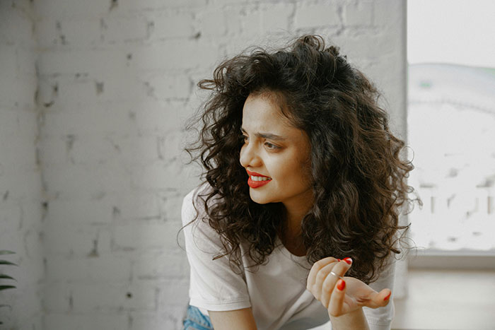 Young woman with curly hair and red lipstick, appearing engaged in a conversation.