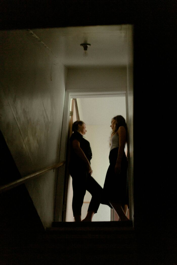Two women standing in a dimly lit stairway, illustrating a potentially traumatizing experience.