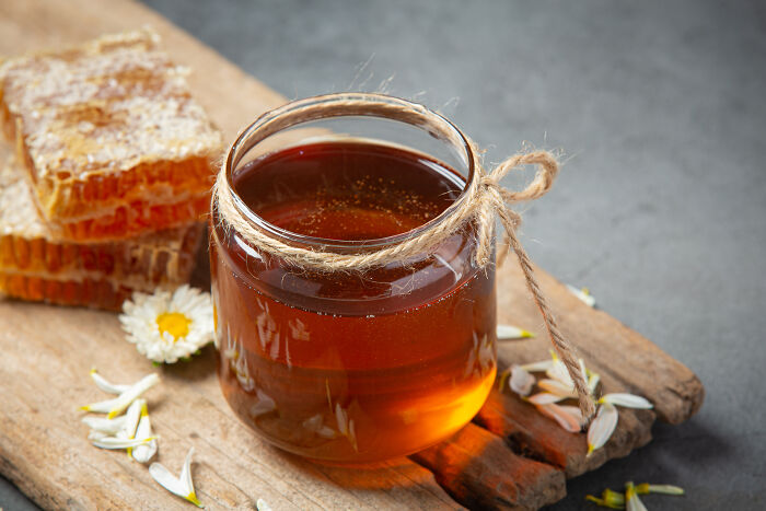 Jar of honey with honeycomb on a wooden board, surrounded by flower petals; a unique gift idea for someone with everything.