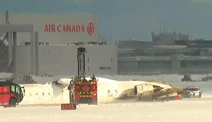 Delta Airlines plane flipped upside down post-crash landing, emergency vehicles present. Delta Airlines plane flipped upside down post-crash landing, emergency vehicles present.