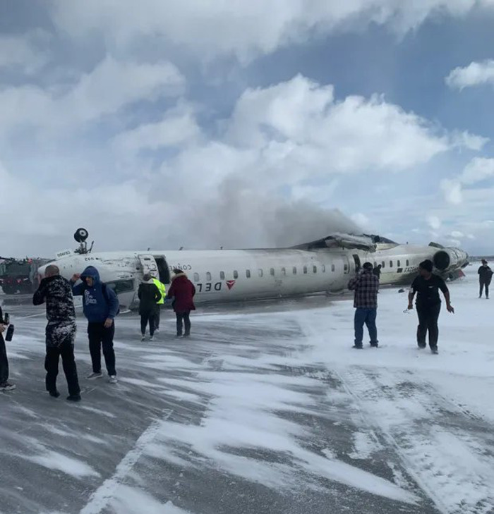 Delta Airlines plane upside down on snowy runway after crash landing, with people nearby. Delta Airlines plane upside down on snowy runway after crash landing, with people nearby.