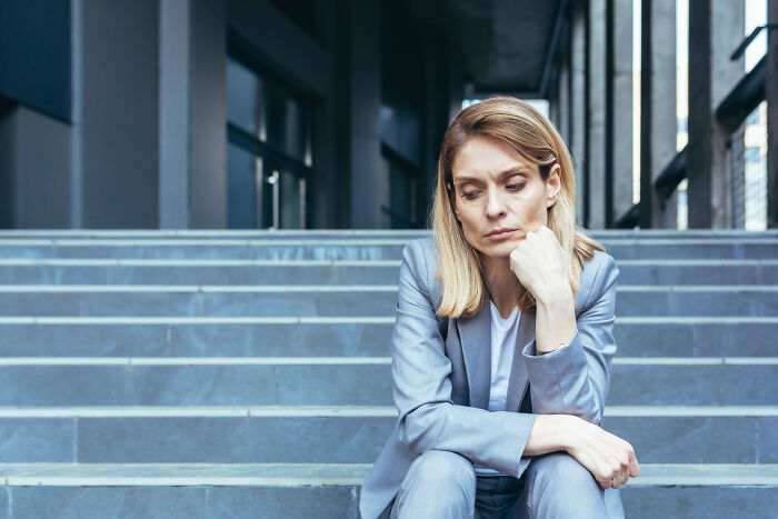 Woman in a blue suit sitting on steps, looking contemplative, reflecting the hardest harsh realities about life.