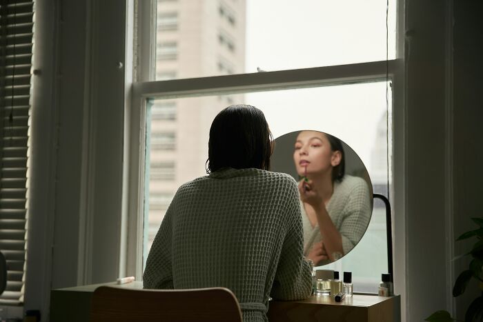 Person applying makeup in front of a window, representing life improvement habits.