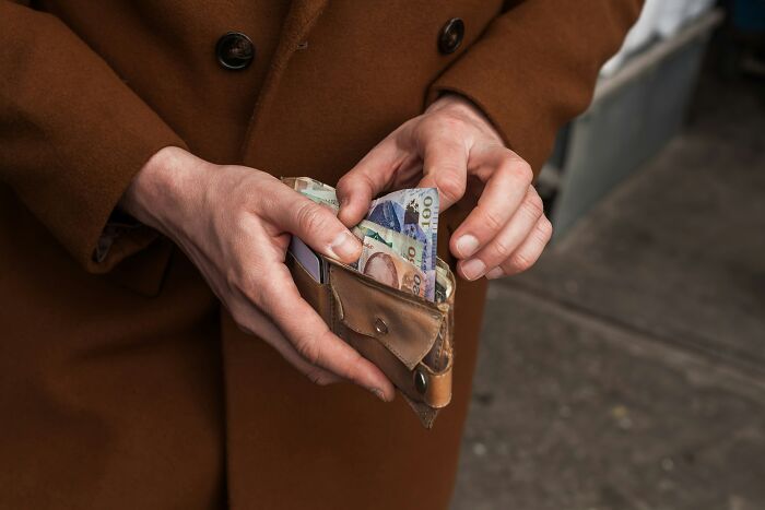 Person in a brown coat holding a wallet with various bills, illustrating a memory tied to their father.