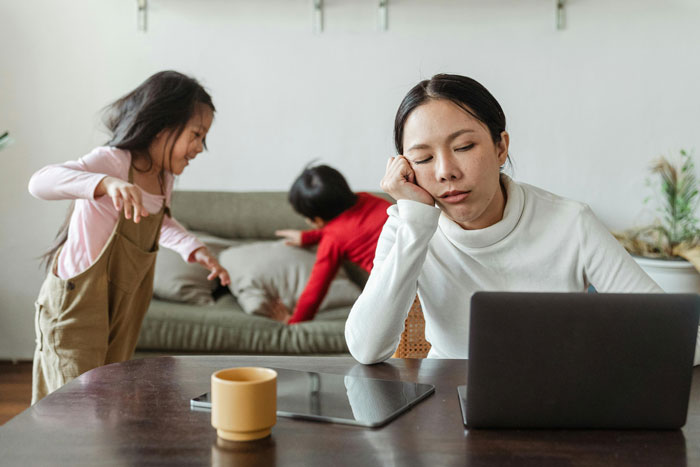 Mother stressed at table while kids throw tantrums; family trip struggles. Mother stressed at table while kids throw tantrums; family trip struggles.