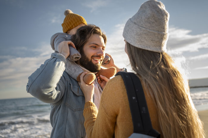 Family enjoying a beach day, smiling with child on shoulders, capturing a peaceful moment before Disneyland trip tantrums occur. Family enjoying a beach day, smiling with child on shoulders, capturing a peaceful moment before Disneyland trip tantrums occur.