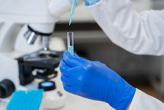 Lab technician using DNA testing equipment, holding a pipette and test tube.