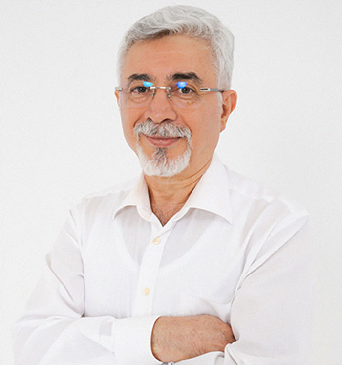 Man smiling with arms crossed, wearing glasses and a white shirt, related to Bianca Censori's plastic surgery makeover topic.
