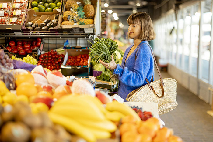 Woman selecting fresh greens in a vibrant grocery store produce section.