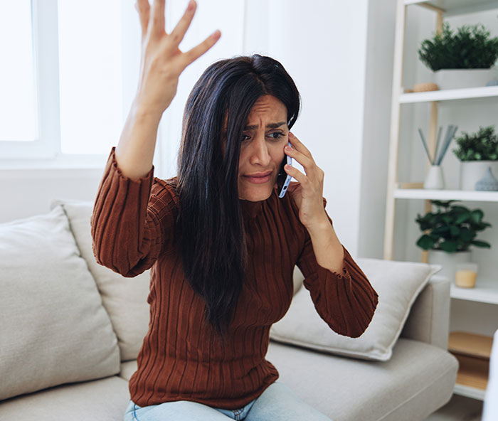 Woman on phone looking upset, sitting on a couch, raising hand in frustration. Woman on phone looking upset, sitting on a couch, raising hand in frustration.
