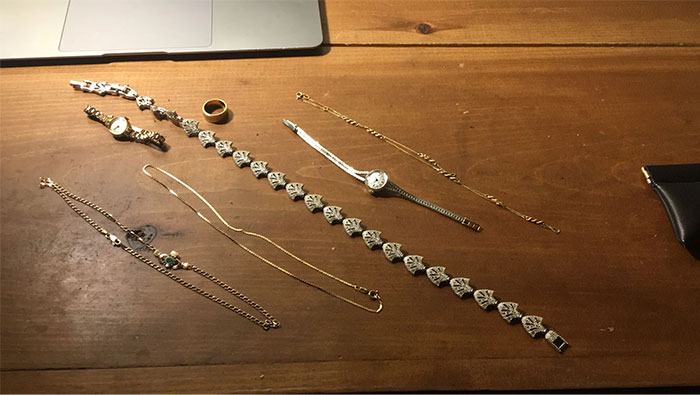 Gold jewelry and watches found while dumpster diving displayed on a wooden table.