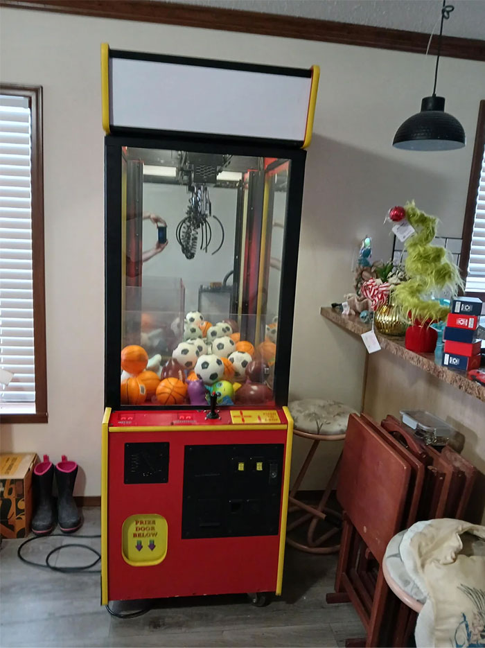 Claw machine with toys found while dumpster diving, displayed in a room with wooden furniture.