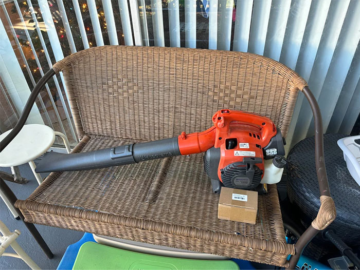 Leaf blower found while dumpster diving, placed on a wicker bench on a patio with vertical blinds in the background.