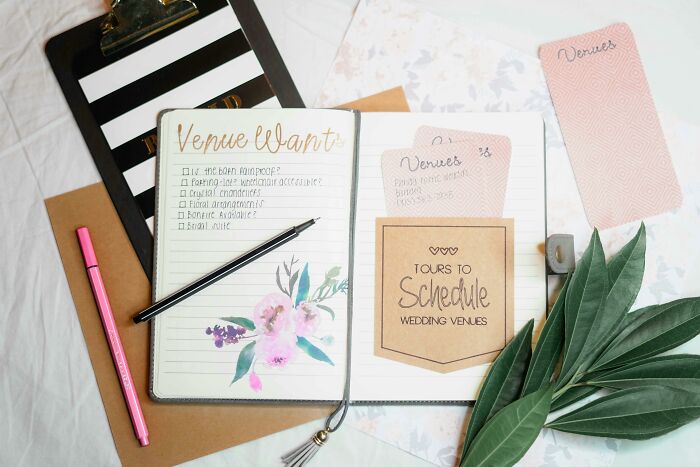 Wedding planning notebook with venue ideas, open with notes and decorations, pen, and flowers nearby.