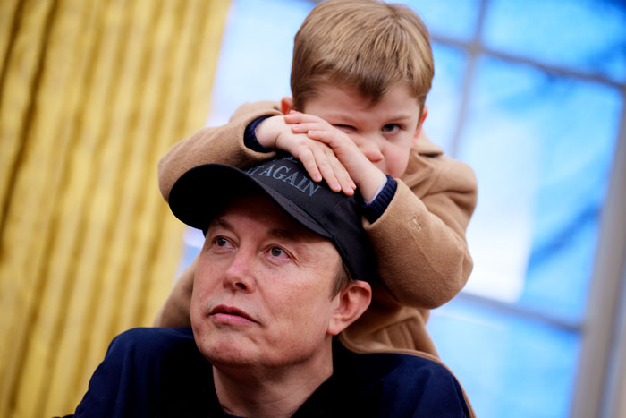 Man wearing a cap with a child on his shoulders, indoors with curtains and a window in the background, related to Elon Musk. Man wearing a cap with a child on his shoulders, indoors with curtains and a window in the background, related to Elon Musk.