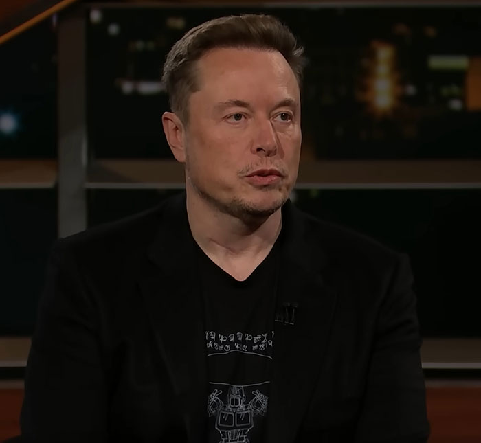 Elon Musk in a dark suit, seated and speaking in a studio setting. Elon Musk in a dark suit, seated and speaking in a studio setting.