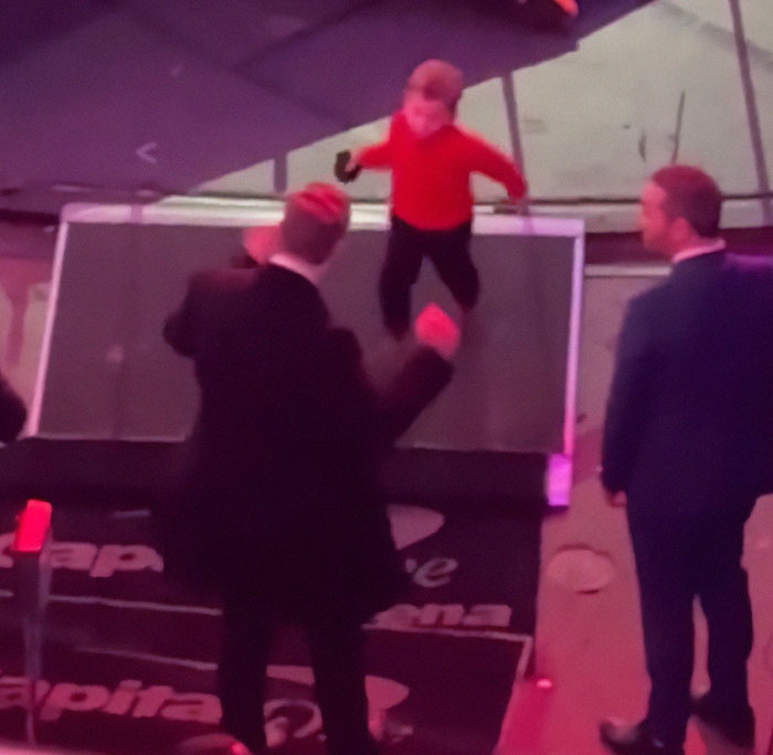 Elon Musk in a suit on stage with a child in a red shirt, related to discussions of leaving behind son X.