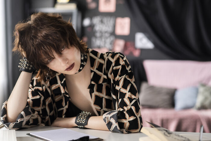 Person sitting thoughtfully, wearing a patterned shirt and spiked accessories, reflecting on unforgettable words from their father.