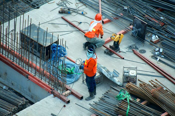 Construction workers at a building site surrounded by metal rods and equipment, related to anticipated price hikes.