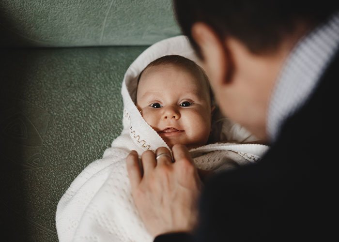 Man holding a smiling baby wrapped in a white blanket, focusing on the baby's expression.