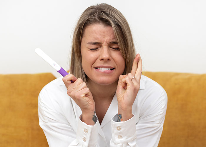 Woman holding pregnancy test with fingers crossed, expressing emotion and honesty.
