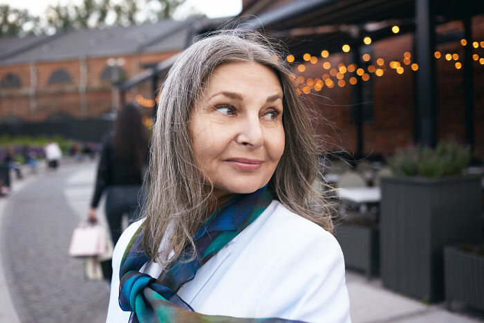 Senior woman outdoors in white blouse and scarf, representing women sharing about offensive remarks.