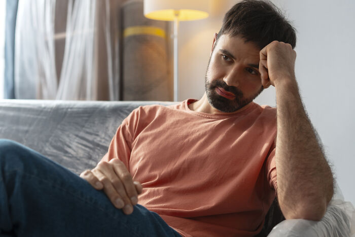 A man in a pink shirt sitting pensively on a sofa, symbolizing unforgettable words from a father.