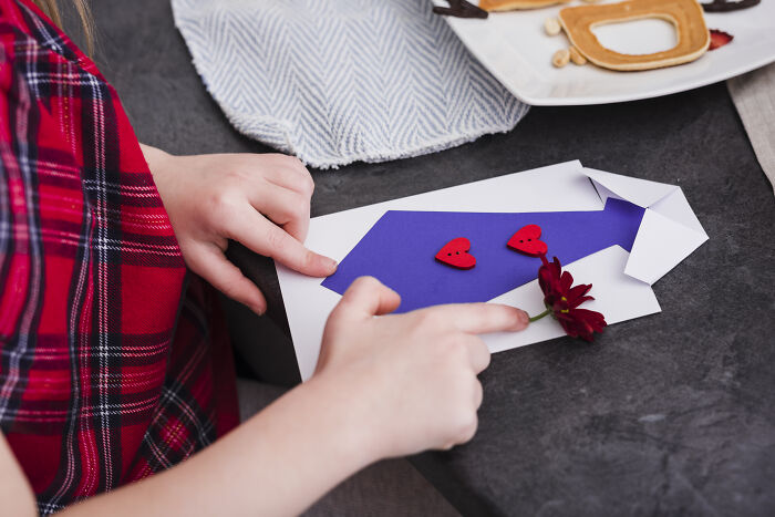 Child making a simple and adorable Valentine's gift with paper craft on a table.