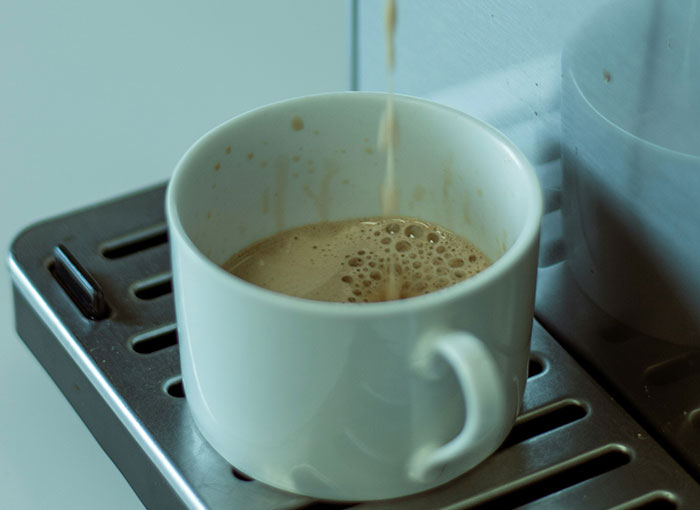 Coffee being poured into a white mug on a metal drip tray.