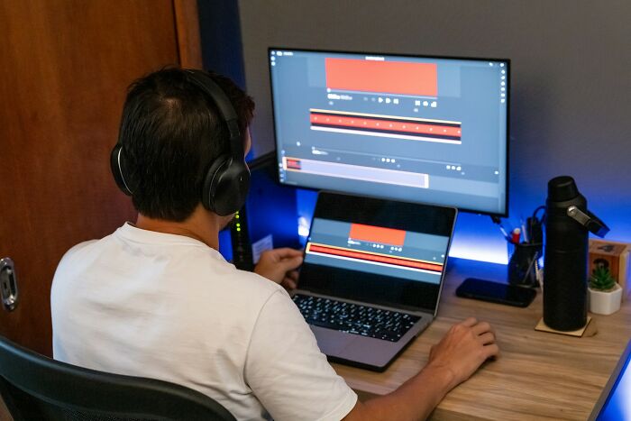 Person using dual screens for video editing, wearing headphones, highlighting industry professions in tech.