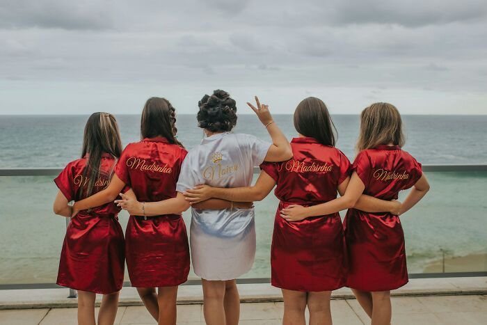 Bridesmaids in red and a bride in white, facing the ocean, highlighting common wedding complaints from guests.