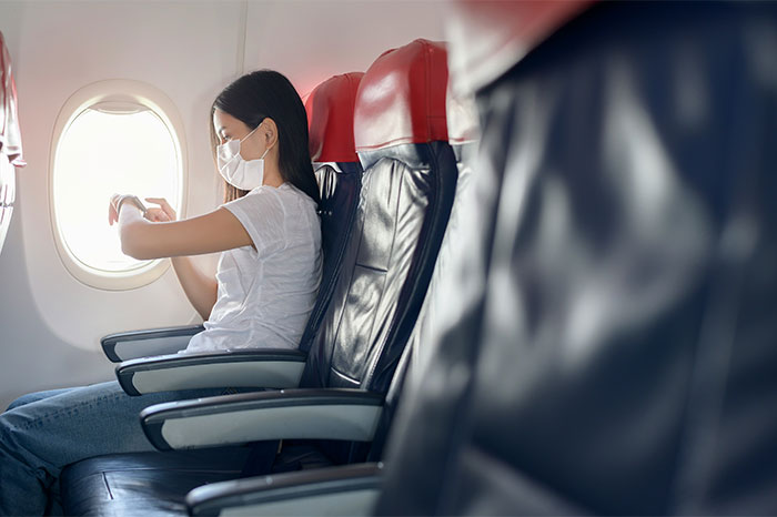 Passenger wearing a mask on a plane, observing flying etiquette by keeping the window shade open.
