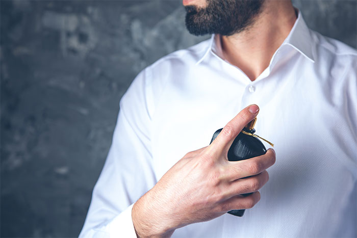 Man in a white shirt spraying cologne, related to flying etiquette rules.