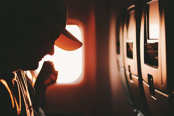 Passenger seated on an airplane, silhouetted against a window, highlighting flying etiquette.