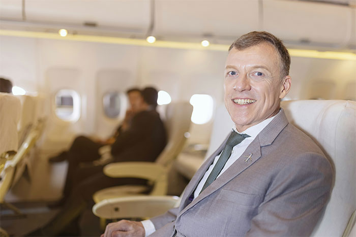 Smiling passenger in a suit seated on an airplane, illustrating flying etiquette in travel settings.