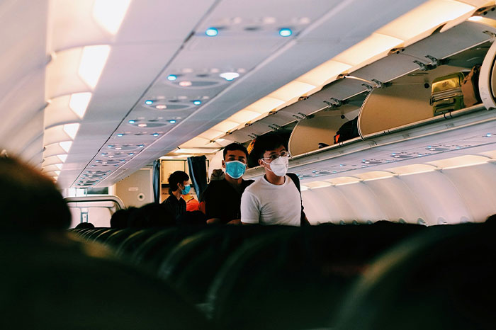 Passengers on a plane observing flying etiquette, wearing masks, while boarding and storing luggage in overhead bins.