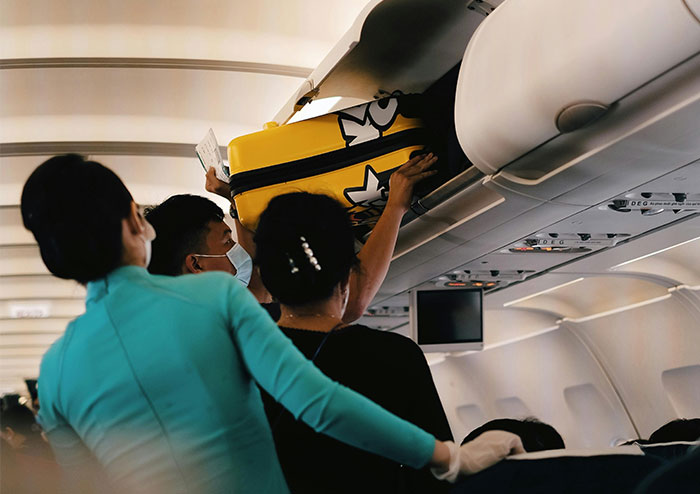 Passengers storing luggage in an airplane overhead bin, demonstrating flying etiquette.