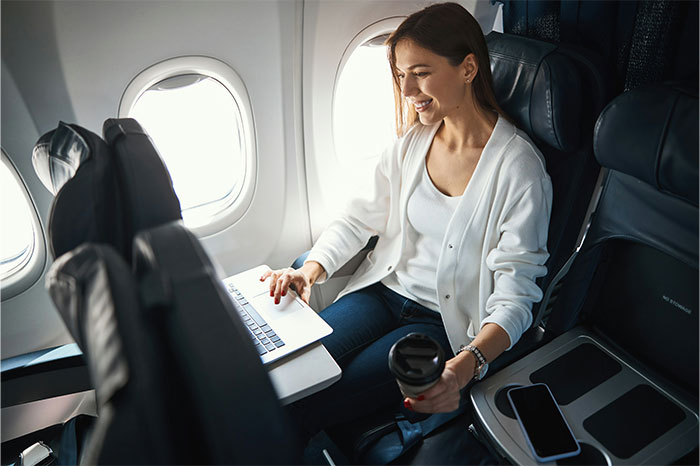 Passenger using a laptop on a flight, holding a coffee cup; highlights flying etiquette.