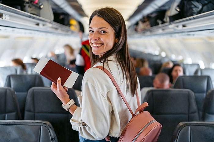 Smiling passenger with a pink backpack holding a passport, highlighting flying etiquette on an airplane.