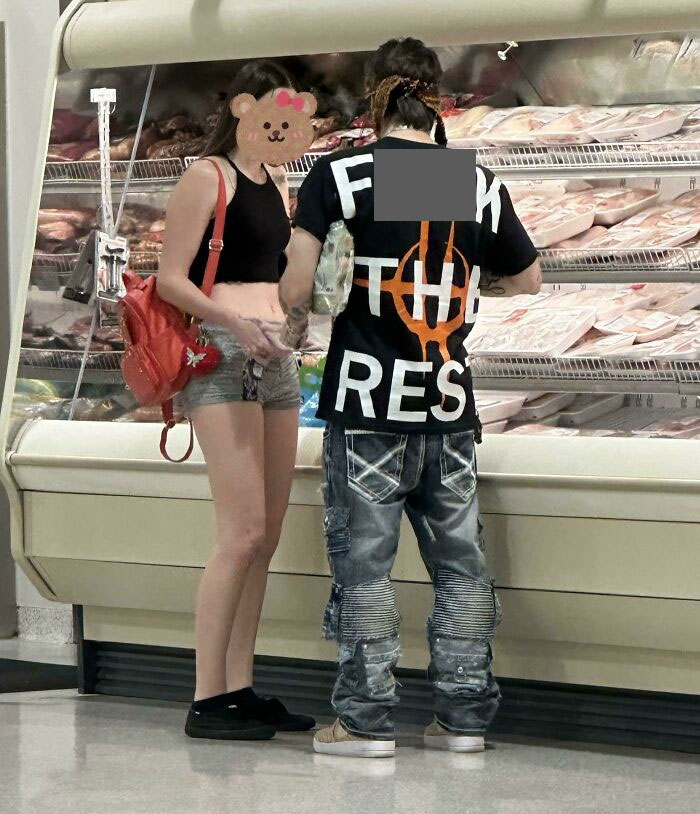 Young couple in casual attire shopping at a Florida deli counter, showcasing unique fashion choices.