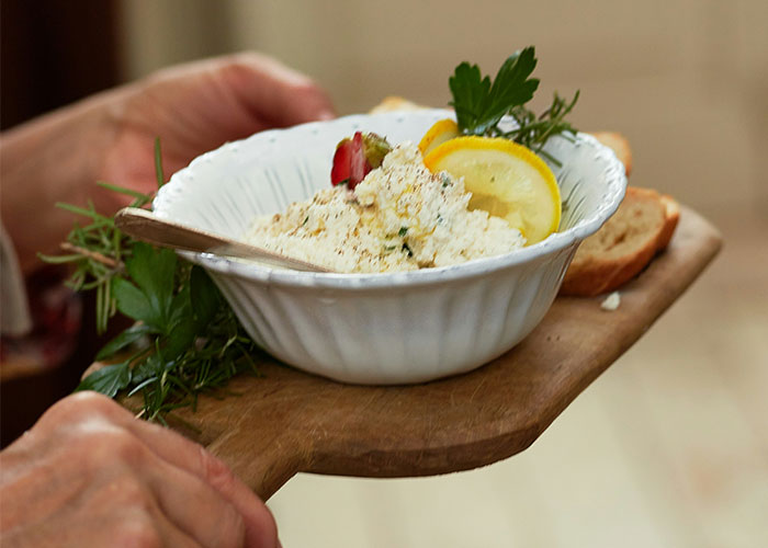 Bowl of garnished ricotta cheese on a wooden board with herbs and lemon, reflecting foods loved by adults.