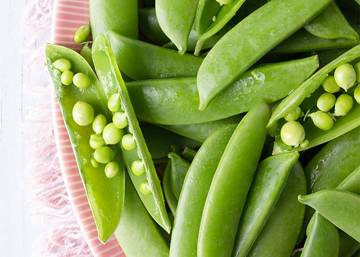 Fresh sugar snap peas on a pink plate, highlighting foods that people started loving when they grew up.