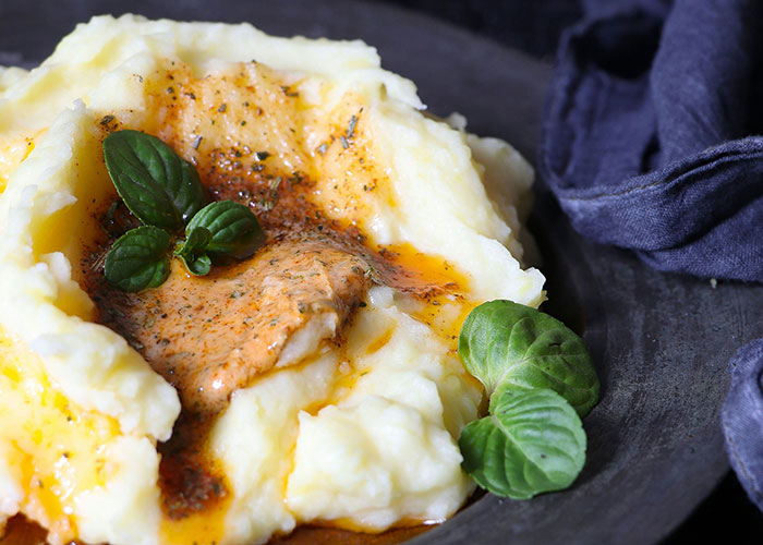 Mashed potatoes with herb butter and basil leaves on a dark plate.
