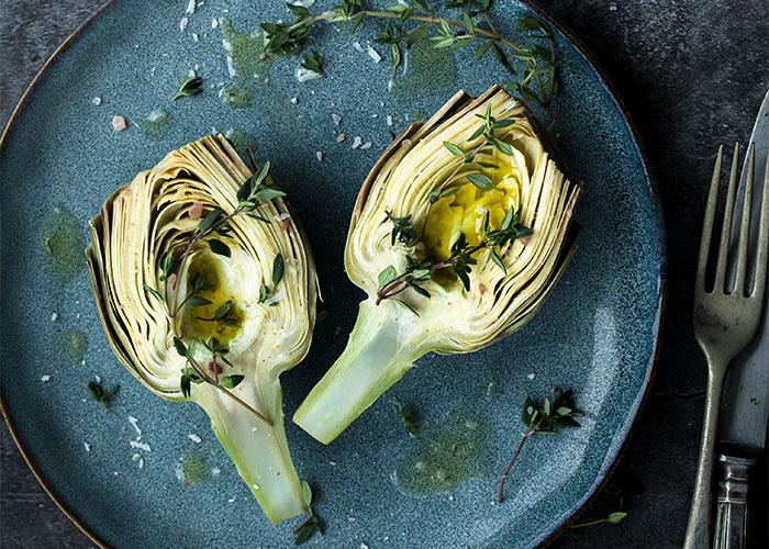 Artichokes garnished with herbs on a blue plate. Foods people love as adults.