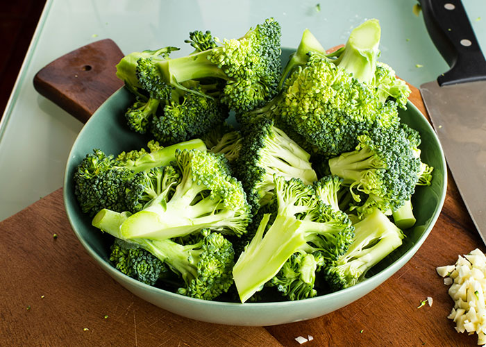 Bowl of fresh broccoli on a wooden board, representing foods that people started loving when they grew up.