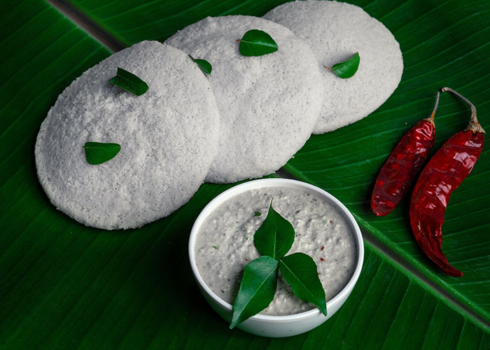 Idli with chutney and chillies on banana leaves, showcasing foods people love as they grow up.