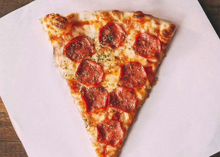 Slice of pepperoni pizza on a white surface, representing foods people started loving as they grew up.
