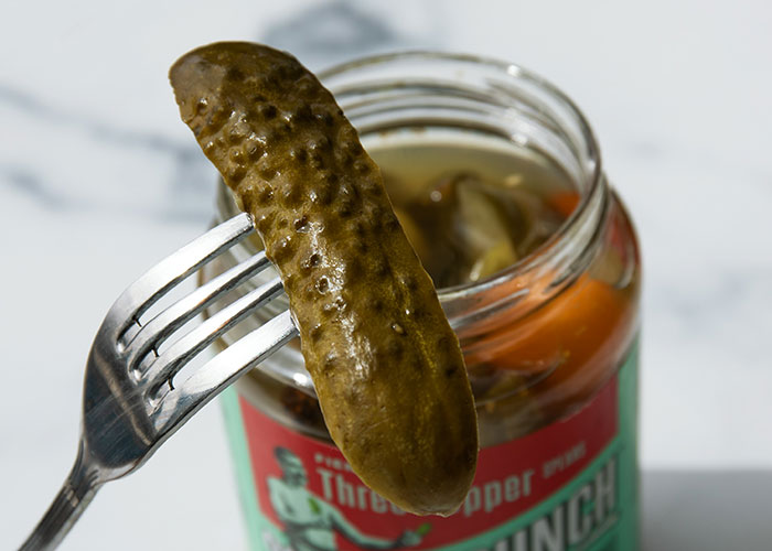 Pickle lifted on a fork from a jar, illustrating a food that people started loving as they grew up.