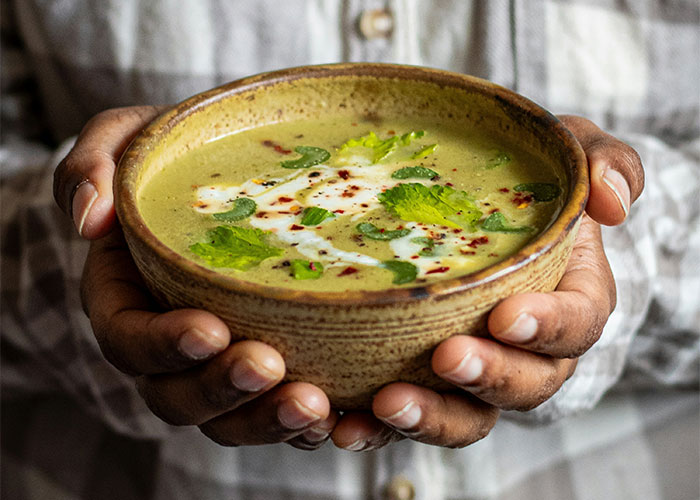 Hands holding a bowl of soup with cilantro and cream, representing foods people love as adults.